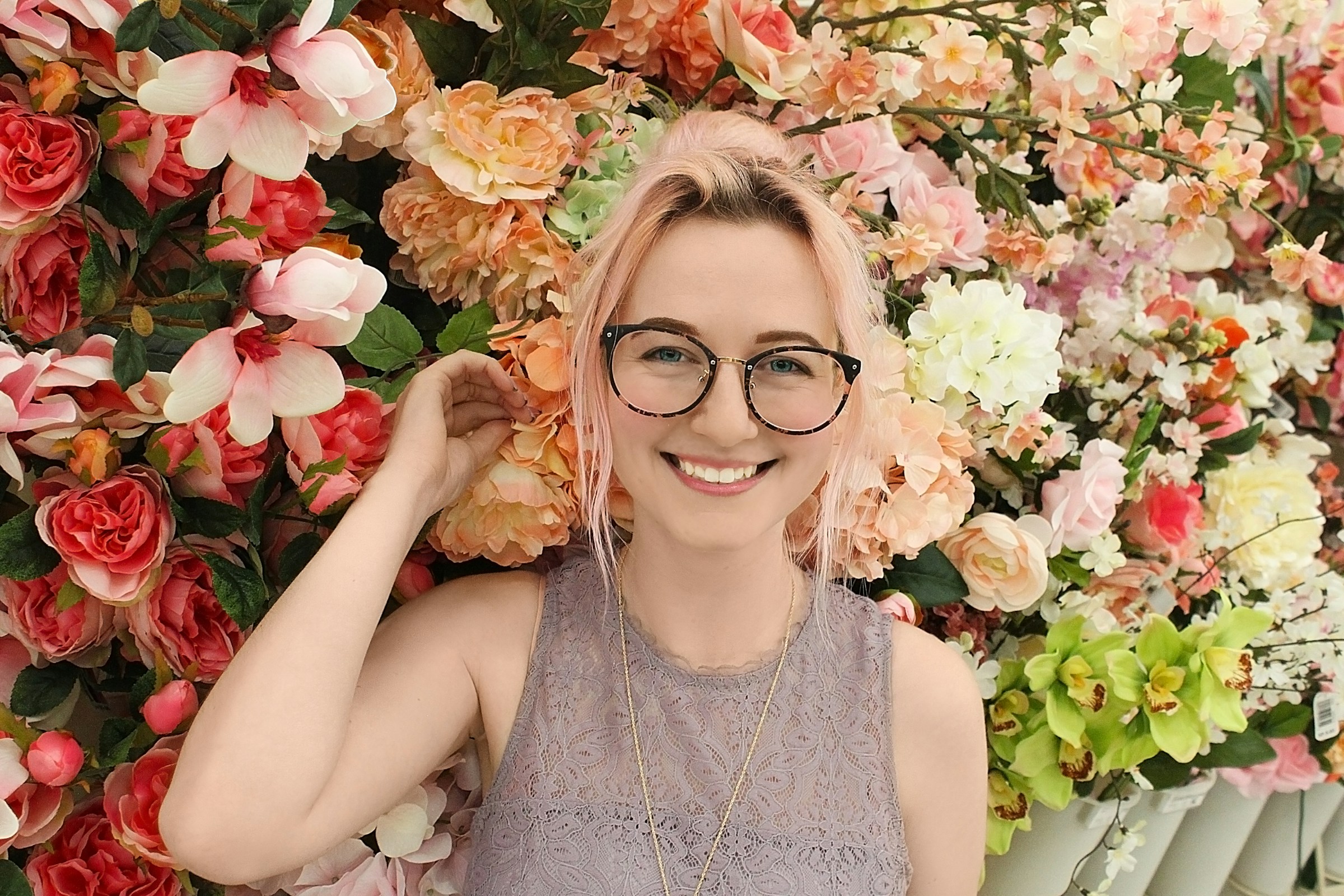 a model wearing glasses posing in front of a flower wall